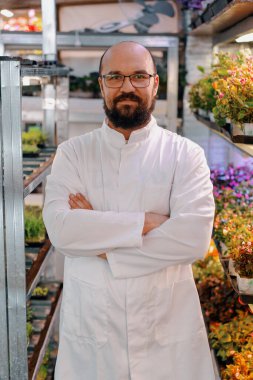 Gözlüklü ve beyaz önlüklü gülümseyen erkek bahçıvanın portresi mikroyeşil çiftlik sağlıklı vegan besin organik bitki yetiştirme