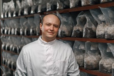 Mantar çiftliği, gülümseyen bilim adamı-mikolog plastik torbalarda mantarlarla birlikte organik gıda ürünleri.