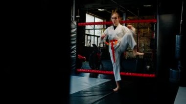 Kimonolu bir kadın olarak karate yapıyor. Hareketler yapıyor ve dövüş sanatlarında poz veriyor.