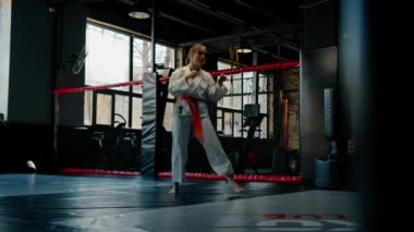 Kimonolu bir kadın olarak karate yapıyor. Hareketler yapıyor ve dövüş sanatlarında poz veriyor.