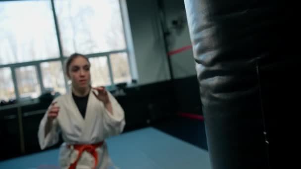 空手の武道を学びながら ジムでパンチングバッグと着物の練習の女の子 — ストック動画