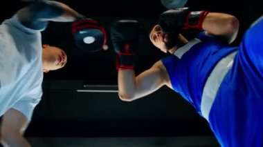 Boks eldivenli sporcu boks partnerine aşağıdan yakın plan yumruklar öğretiyor.