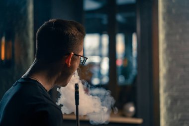 Bardaklı bir nargile adam geleneksel bir nargile piposu tüttürür. Bir adam nargile kafesinde ya da bar yakınlarında sigara tüttürür.