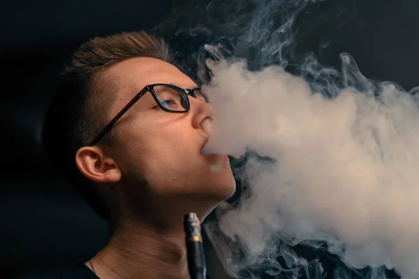 A hookah man in glasses smokes a traditional hookah pipe A man exhales smoke in hookah cafe or lounge bar close-up