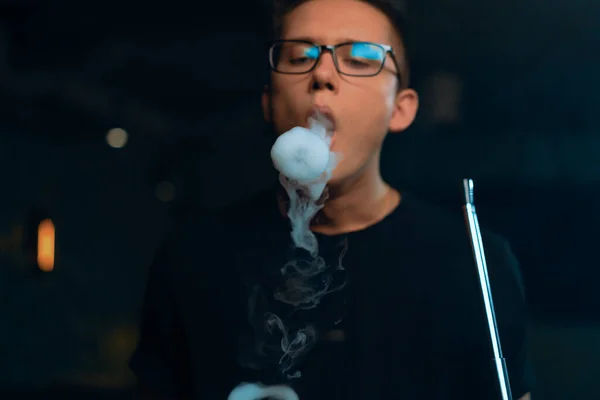 A man in glasses smokes a traditional hookah pipe A man exhales rings of thick smoke in hookah cafe or lounge bar