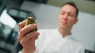 Profesyonel mutfak şefi elinde armut tutuyor ve yemek pişirme konseptini inceliyor.