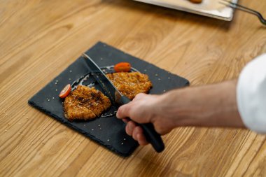 Aşçı mutfakta yemek pişiriyor. Ekmek kırıntılarıyla tavuk filetosu kesiyor.