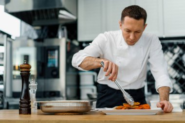 Profesyonel mutfak aşçısı fırında patatesleri maşayla çıkarıp tabağa koyar.