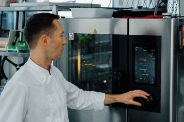 Restorandaki profesyonel modern mutfak aşçısı dışarı çıkıyor ve fırının parametrelerini ayarlıyor.