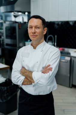 Profesyonel mutfak gülümsemesi ve tatmin olmuş şef beyaz önlüğü çapraz kollu portreyle duruyor.