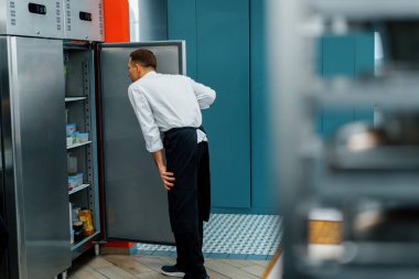 Profesyonel mutfak şefi buzdolabına bakar ve yemek pişirme konsepti için malzeme seçer.