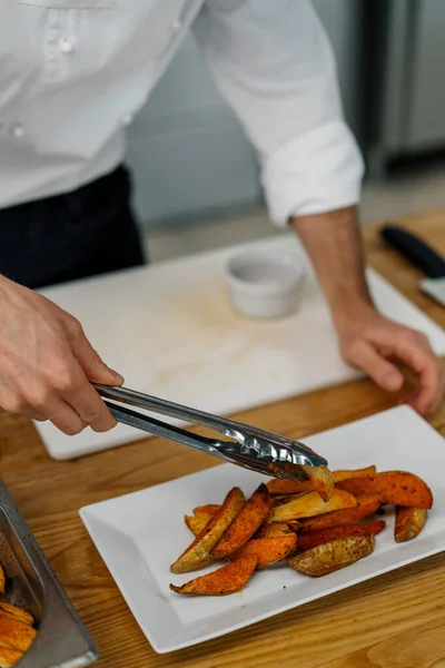 プロのキッチンシェフは トングとスパイスと焼きジャガイモを取り出し プレートに置きます — ストック写真