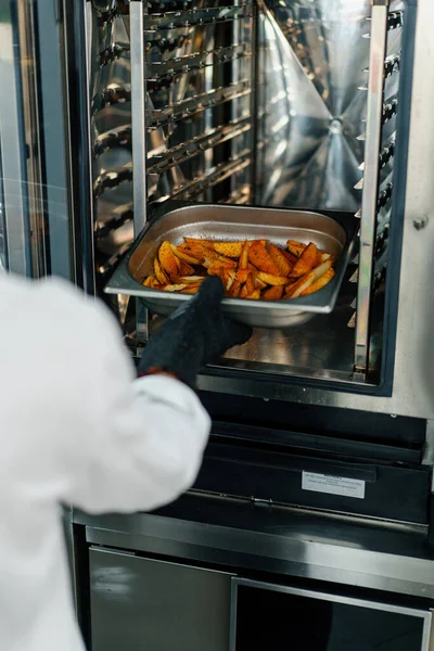 プロのキッチンシェフはオーブン調理プロセスから焼きジャガイモとベーキングトレイを取り出します — ストック写真