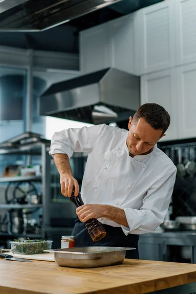 プロのキッチンシェフはオーブンで焼く前にベーキングトレイのジャガイモの部分に調味料を追加します — ストック写真