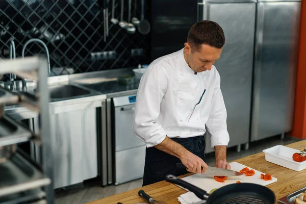 プロのキッチンシェフが新鮮なジューシーな赤いトマトをナイフで切ってテーブルの上に野菜を閉じます — ストック写真