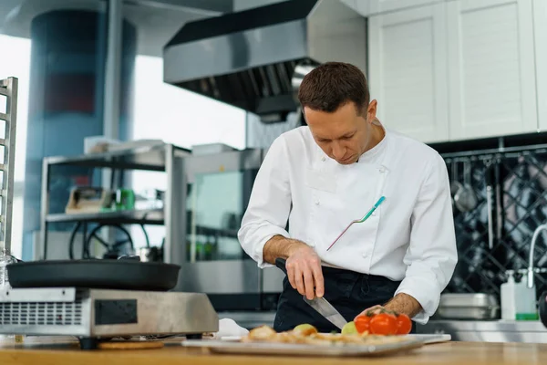 プロのキッチンシェフは ナイフで新鮮なジューシーな緑のアボカドを切り取りますクローズアップ野菜テーブル — ストック写真