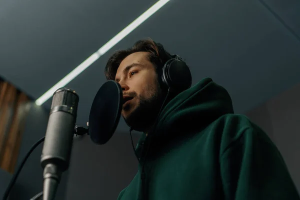 Kulaklık ve mikrofonlu şarkıcı profesyonel kayıt stüdyosunda duygusal olarak yeni bir şarkı kaydediyor.