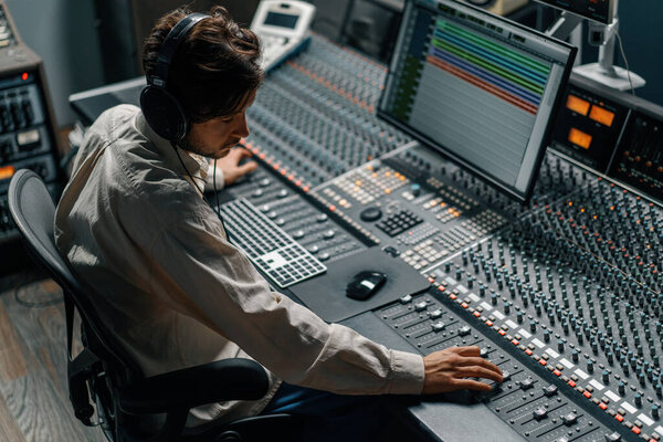 Звукорежиссер, работающий в музыкальной студии с мониторами и эквалайзером