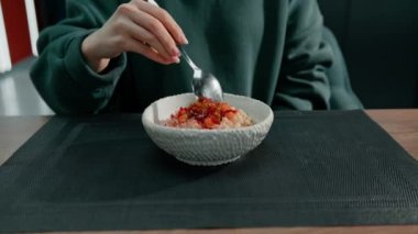 Lokantadaki kız taze yulaf ezmesi yiyor ve karamelli meyveli kahvaltıyı yakından çekiyor.