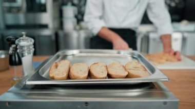 Profesyonel modern restoran mutfak aşçısı fırın tepsisinde kızartılmak üzere taze ekmek dilimleri serer.