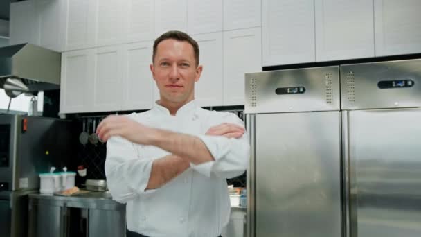 プロのキッチン笑顔と満足シェフ白いコートの横に立って腕の肖像画 — ストック動画