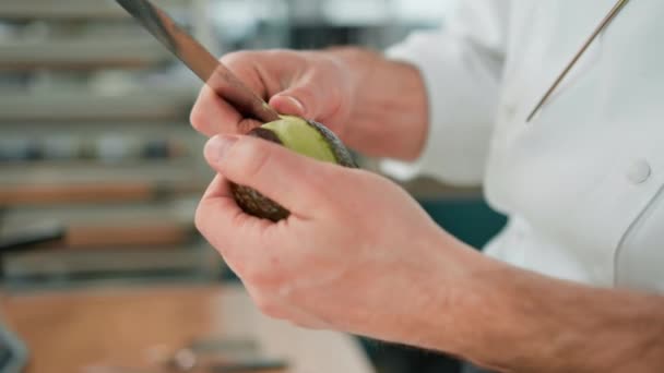 プロのキッチンシェフは ナイフで新鮮な緑のアボカドをきれいにすると肌のクローズアップを削除します — ストック動画