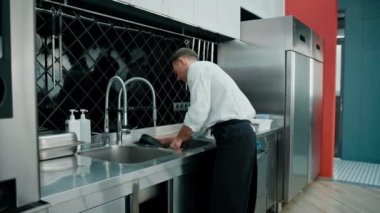 Mutfakta yemek pişirdikten sonra kirli bulaşıkları lavaboda yıkayan profesyonel bir aşçı.