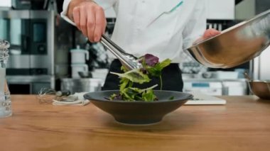 Profesyonel mutfak aşçısı armut ve peynirli salata yapraklarını maşayla karıştırır sağlıklı yemek malzemelerini karıştırır.