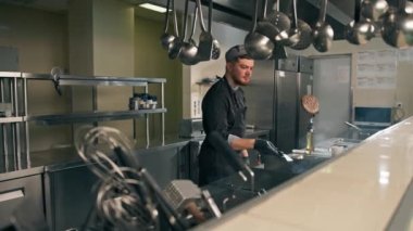 Otel restoranında profesyonel bir mutfak. Şef havada spatulayla hamburger köftesi çeviriyor.