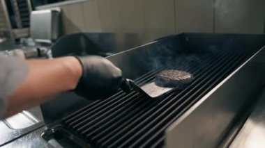 Otel restoranında profesyonel bir mutfak. Şef havada spatulayla hamburger köftesi çeviriyor.
