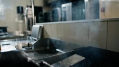 Otel restoranında profesyonel bir mutfak. Şef havada spatulayla hamburger köftesi çeviriyor.