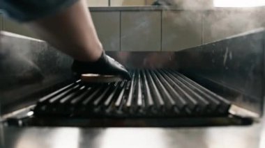 Otel restoranındaki profesyonel mutfak aşçısı ızgaraya hamburgerli çörek koyar.