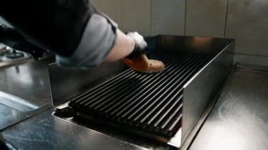 Otel restoranındaki profesyonel mutfak aşçısı ızgaraya hamburgerli çörek koyar.