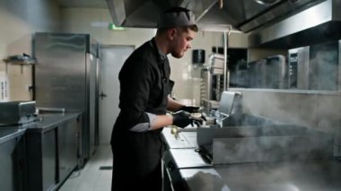 Otel restoranındaki profesyonel mutfak aşçısı ızgaraya hamburgerli çörek koyar.