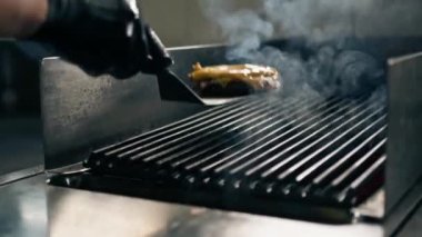 Bir otel restoranında profesyonel mutfak. Şef bir parça peynirli spatulayla hamburger köftesi alıyor.