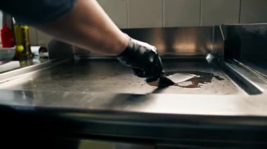 Bir otel restoranında profesyonel mutfak. Şef ızgarayı spatulayla yağlıyor.