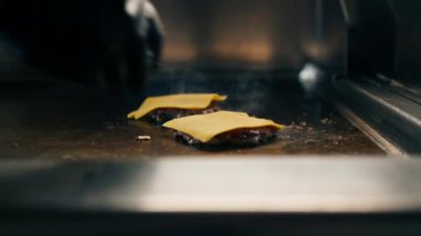 Bir otel restoranında profesyonel mutfak, yakın plan, şef ızgara hamburgerin üzerine peynir dilimleri koyar.
