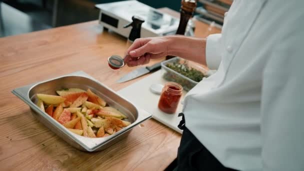プロのキッチンシェフはオーブンで焼く前にベーキングトレイのジャガイモの部分に調味料を追加します — ストック動画