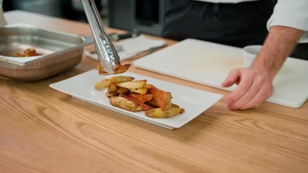 プロのキッチンシェフは トングとスパイスと焼きジャガイモを取り出し プレートに置きます — ストック動画