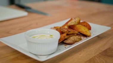 Profesyonel mutfak ekşi krema sosu ve masada baharatlı patates dilimleri.