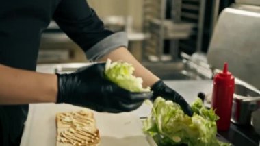 Otel restoranında profesyonel bir mutfak. Şef, tost üzerine kulüp sandviçi için gerekli malzemeleri hazırlıyor.