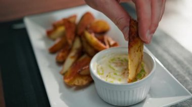 Lokantada bir tabak fırında patates. Avucunda baharatlar var. Ekşi krema sosuna batırılmış.