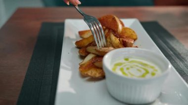 Lokantadaki bir tabak fırında patates dilimlerini baharatla bıçaklar ve onları ekşi krema sosuna batırır.