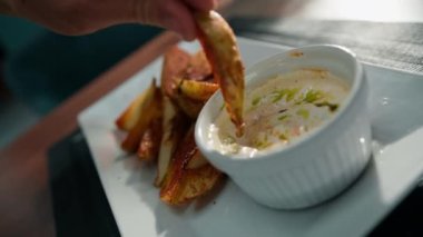 Lokantada bir tabak fırında patates. Avucunda baharatlar var. Ekşi krema sosuna batırılmış.