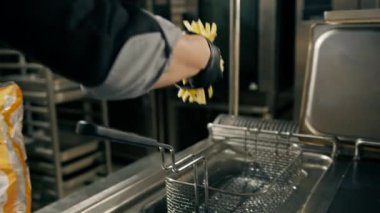 Bir otel restoranında profesyonel bir mutfak. Şef donmuş patates kızartmasını çıkarıp kızgın yağa batırıyor.