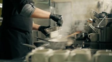Otel restoranındaki profesyonel mutfak tavada ıspanak pişiriyor ve baharat ekliyor.