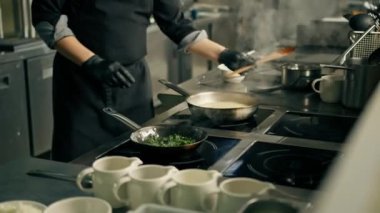 Otel restoranında profesyonel mutfak. Şefin yakın çekimi. Tavada ıspanak hazırlıyor.