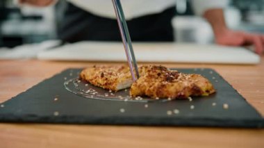 Aşçı mutfakta yemek pişiriyor. Ekmek kırıntılarıyla tavuk filetosu kesiyor.