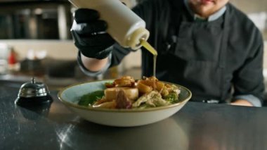 Otelin restoranında profesyonel mutfak, şef deniz ürünleri salatasına baharat sosu döker.