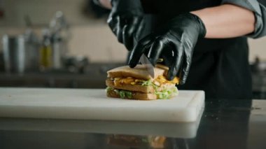 Otel restoranında profesyonel mutfak, şef yeni hazırlanmış iştah açıcı bir kulüp sandviçini bıçakla keser.